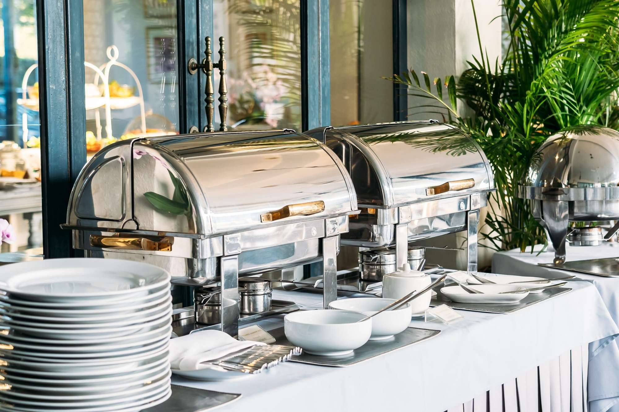 Catering buffet set-up with polished chafing dishes and stacked plates
