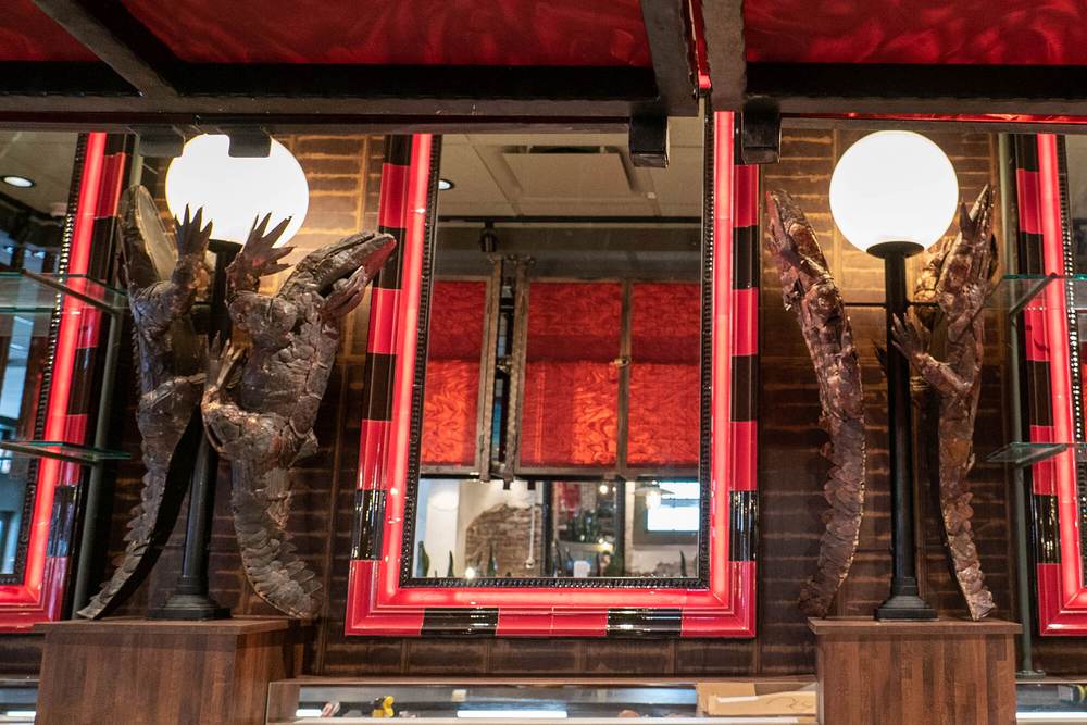 Looking up at the swamp mural ceiling at Mambo's, where two metal alligator sculptures flank a red-lit mirror