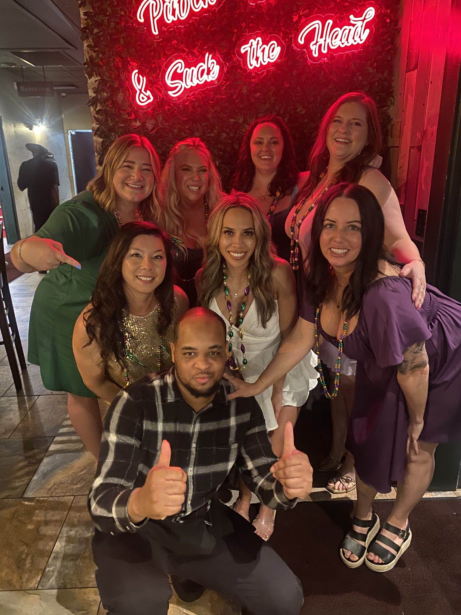 Eight friends in Mardi Gras beads posing under the neon sign at Mambo's